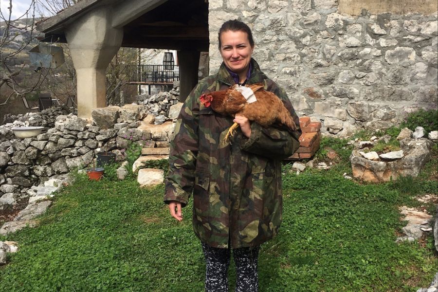 A woman wearing camouflage holds a chicken with a porrly wing