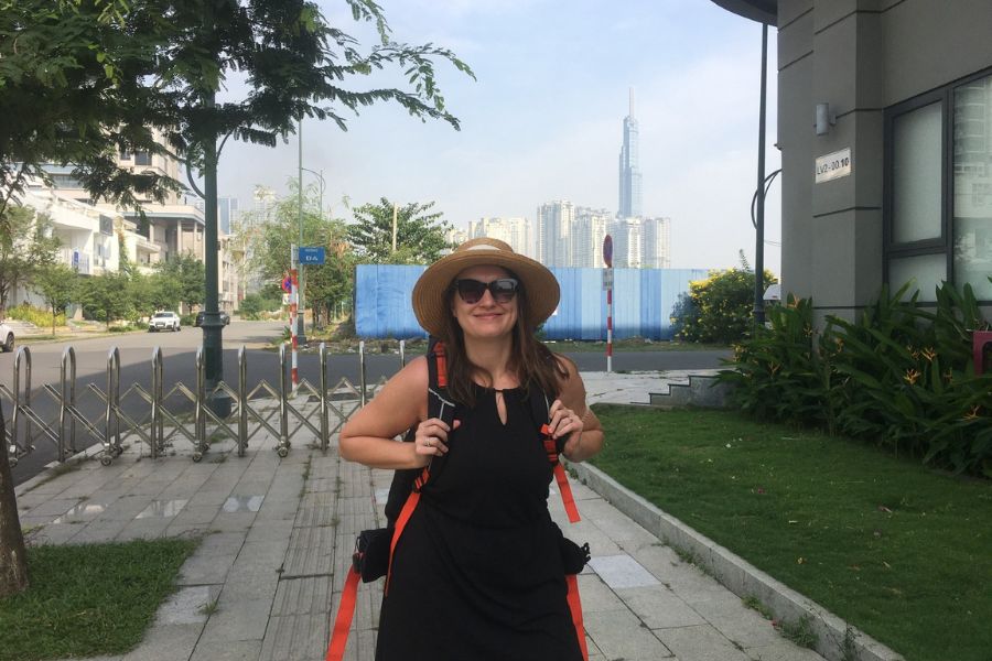 A woman carries a large rucksack standing outside with the Ho Chi Minh City Skyline behind her.