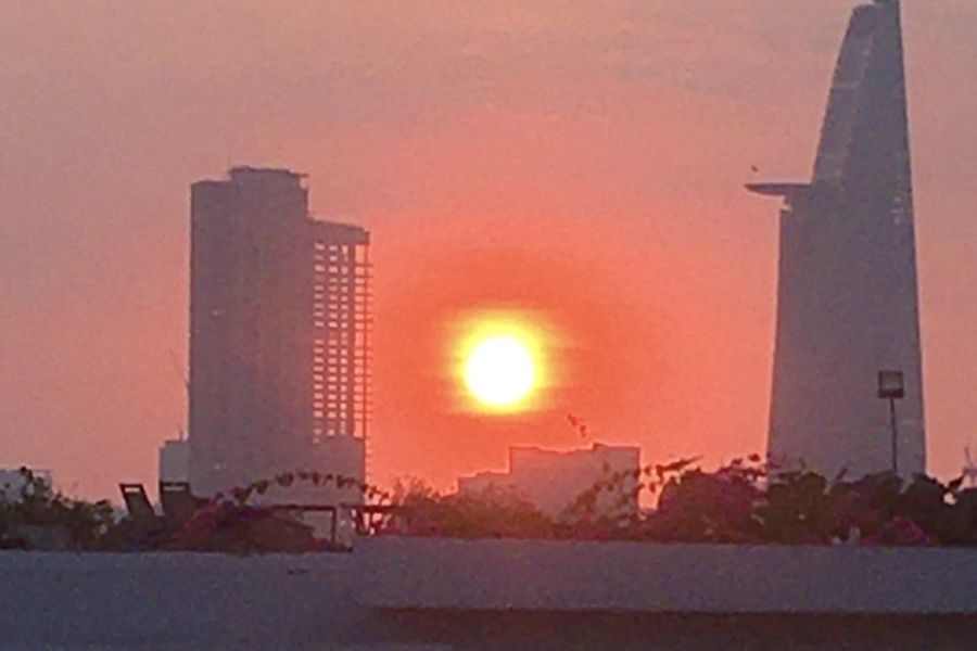 the sun sets between two skyscrapers in Ho Chi Minh City. The large yellow sun is contrasted by an oragne sky