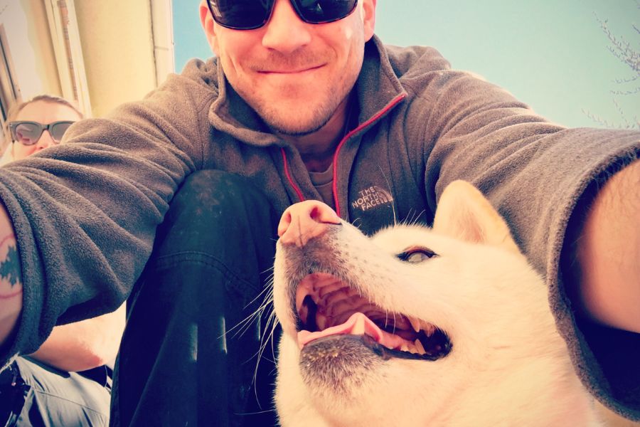 a man in sunglasses smiles for a selfie with a small but fluffy white dog.