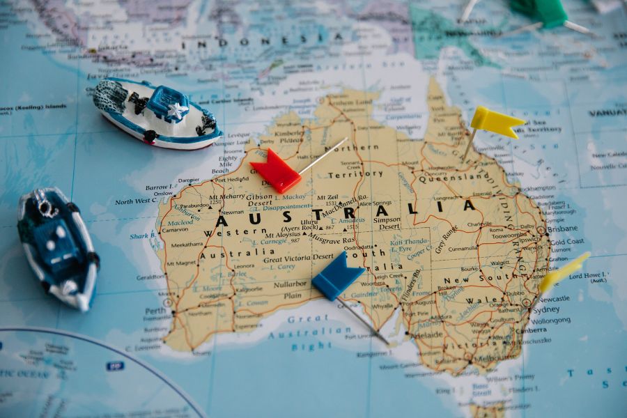 A map showing the entirety of Australia with two figurine boats sailing around it and a couple of colored flags dotted in a few cities.