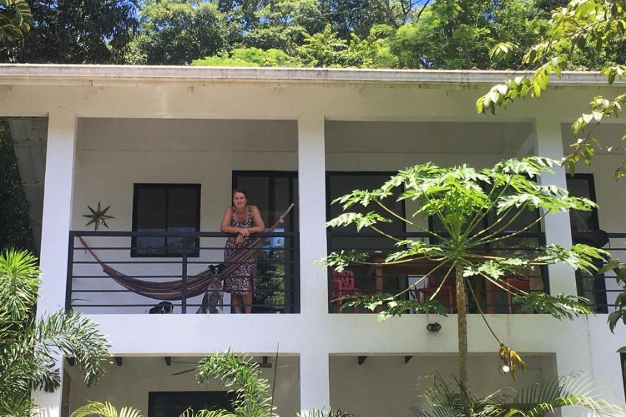 A woman standing on a 1st floor balcony smiling at the camera in a tropical setting.