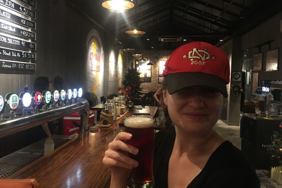 a woman sitting at a bar wearing a red hat holding a pint of beer