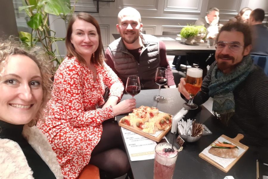 a group of four dults sit around a table enjoying wine, beer, cocktails, and snacks in Brescia, Italy.