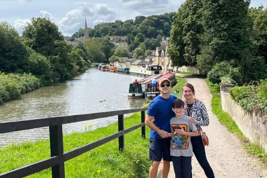 3 peoples, 2 adults and a child stand by the Avon Canal, Riverboats line the banks of the canal.