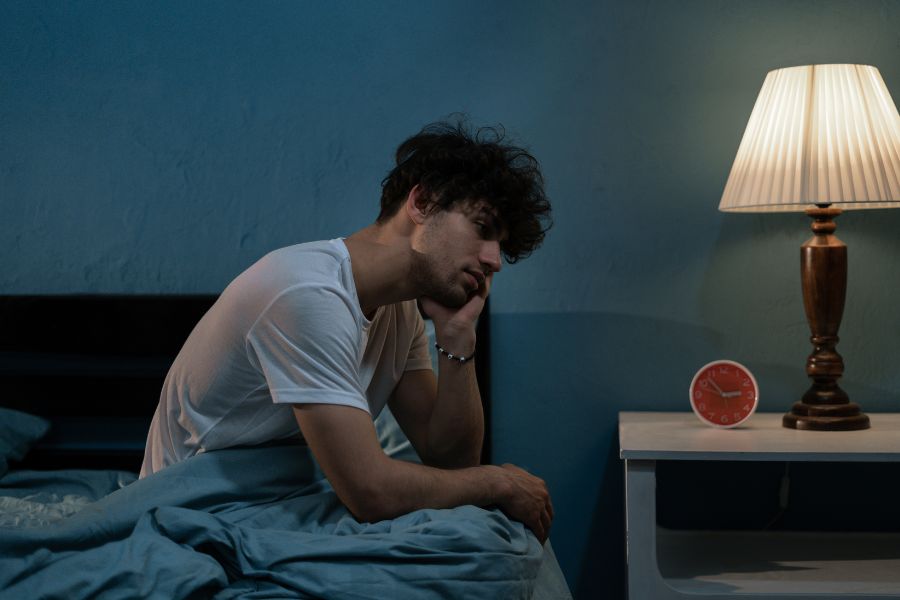 a man sitting on a bed struggling to sleep