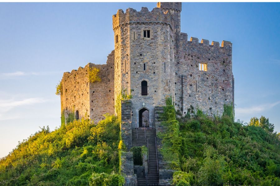 Cardiff Castle. A medieval castle sits atop a green hill in Cardiff. Blue skies light up the lush green hill. 