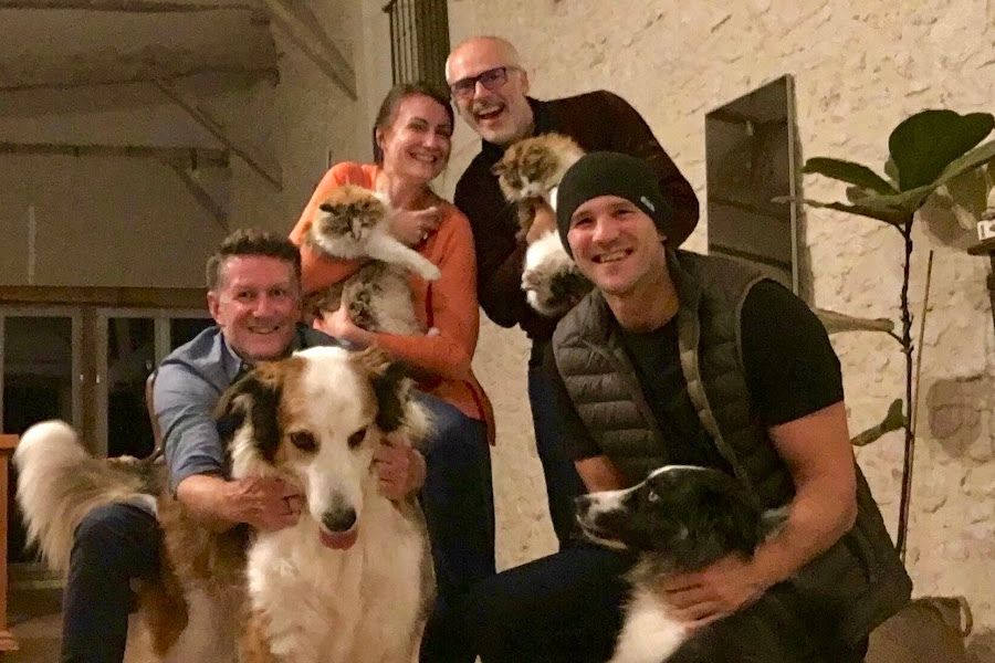 3 men, 1 woman, two dogs and two cats pose for a selfie in a large barn conversion house in France.