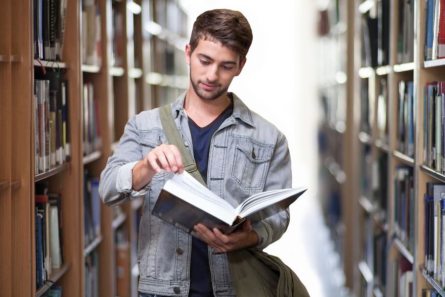 a man reading a big book in a library setting