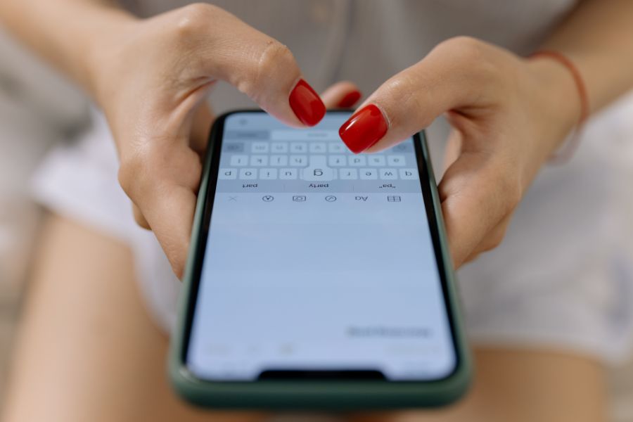 the hands of a woman with red finger nail polish sends a text message