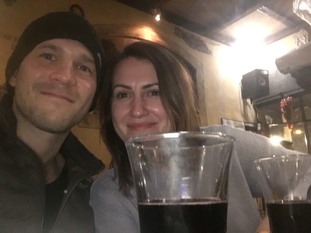 a man and a woman take a selfie with two glasses of red wine in the front of the picture.