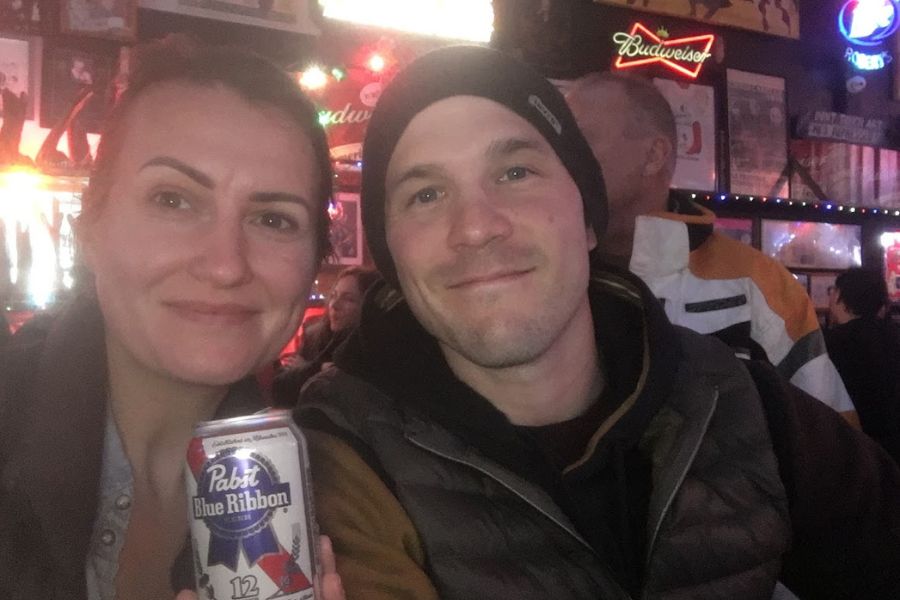 A man and woman take a bar sitting in a neon clad venue in Nashville. The woman is holding a can of PBR in the photo