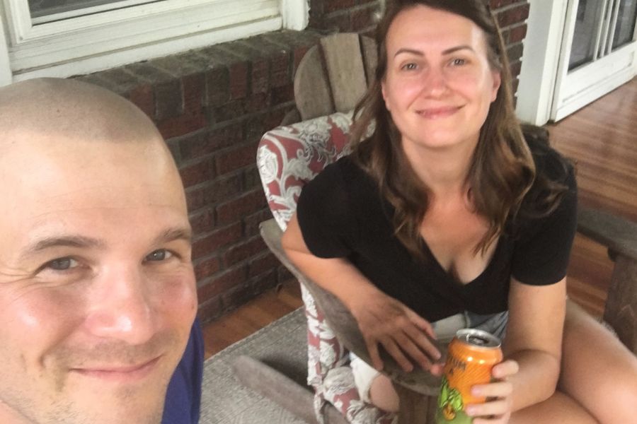 a man and a woman sit on a front porch with a can of beer, taking a selfie