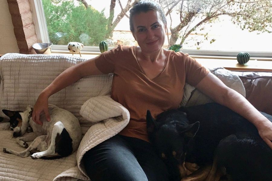 a woman sits on a sofa with 2 sleeping dogs