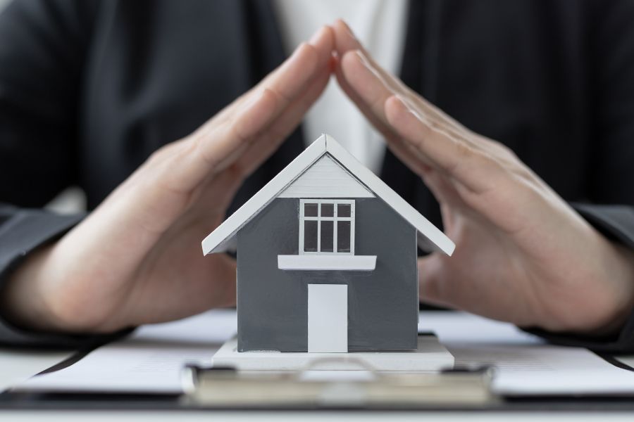 two hands form a roof over a small toy house