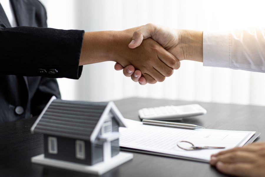 two people shake hands over a small toy house