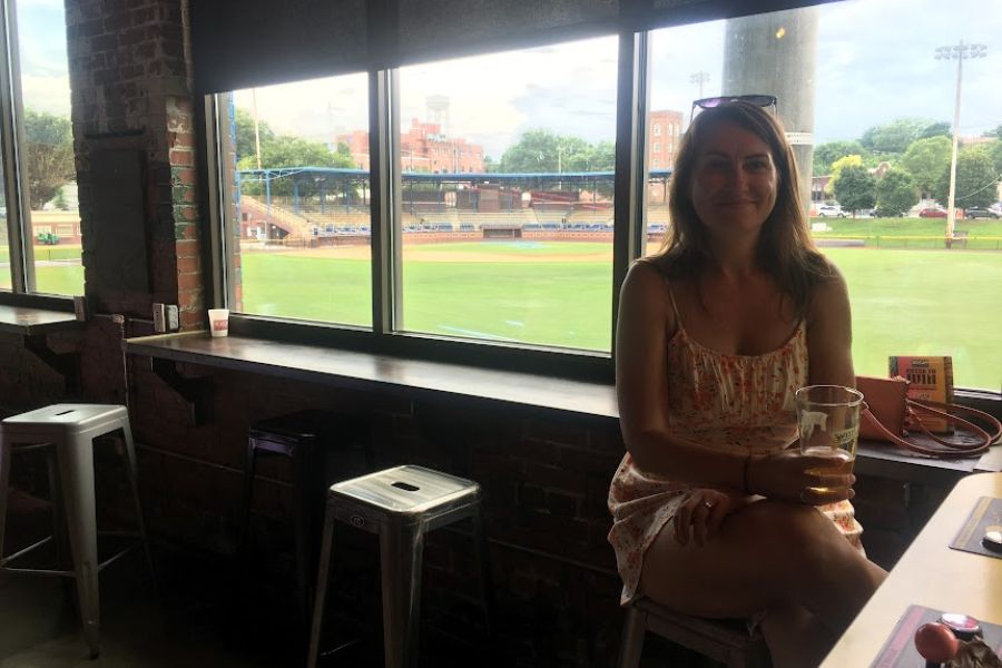 A woman enjoys a beer overlooking a baseball field