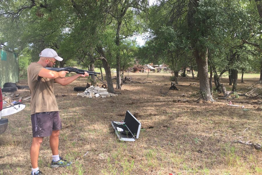 a man aims a shotgun off into the distance on a ranch in Texas