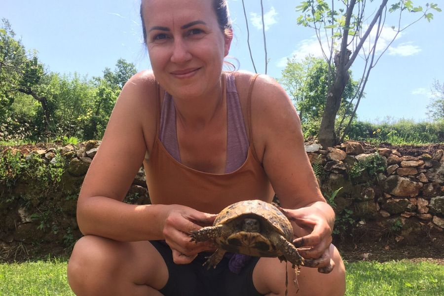 a woman crouches down and holds a tortoise by the shell