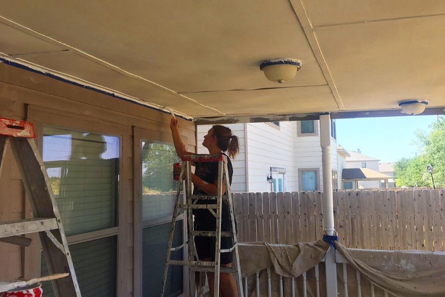 a woman stands on a ladder painting the outside of a house