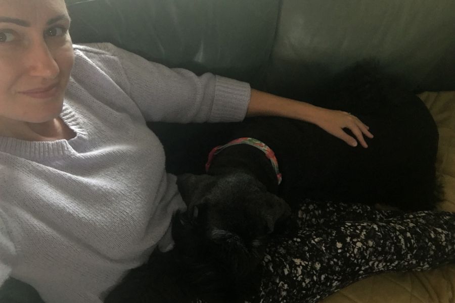 a woman sits on the sofa with a big black dog on her lap