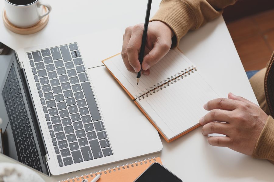 a hand writing on a pad. A laptop also in the picture