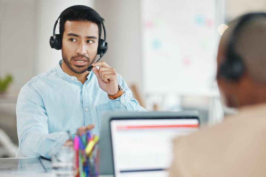 a customer service man speak in to a headset whilst at a computer terminal