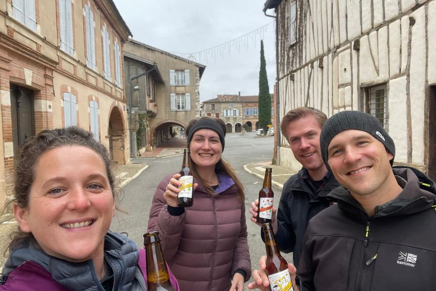 2 men and 2 women pose for a selfie in an outisde bar all holding a bottle of beer