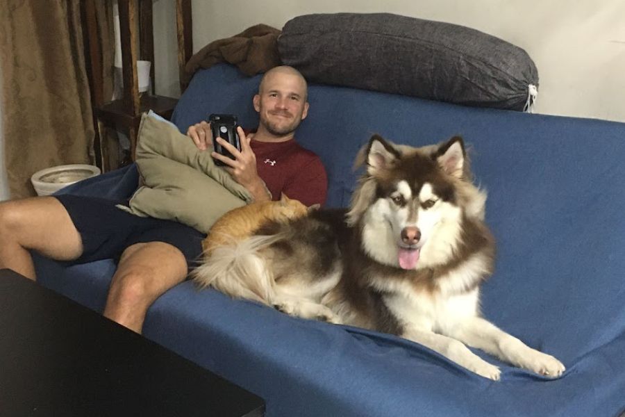 a man, a gold cat and a big husky dog pose for a selfie whilst sitting on a sofa