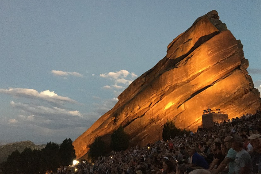 The illuminated rocks at the Red Rocks arena and thousands of fans watching a concert as darkness falls.