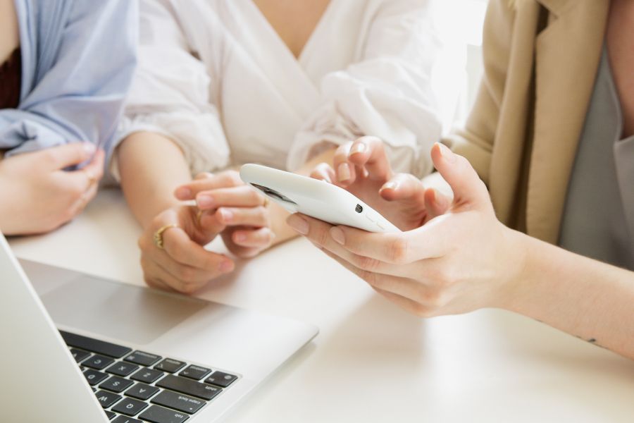 three womens hands clambering around an iphone