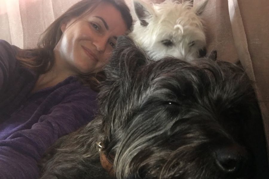 a woman takes a selfie with two cute westies. one white, one black