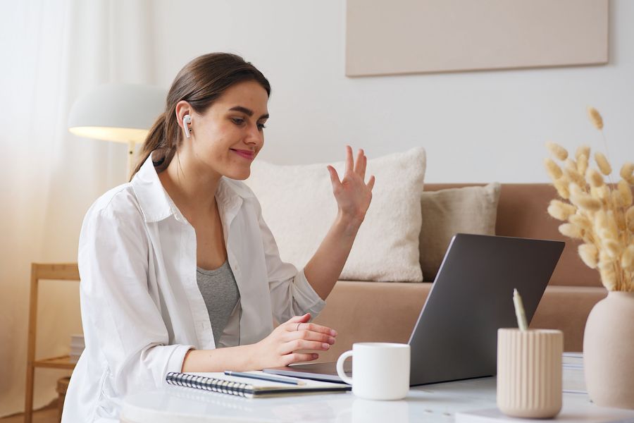 a woman waves to her webcam evidently on a video chat