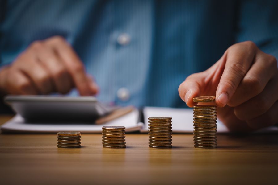 a man with a calculator stacks coins into various piles, evidently working out costs for something