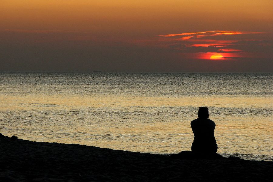 someone sits looking out over the ocean at sunset