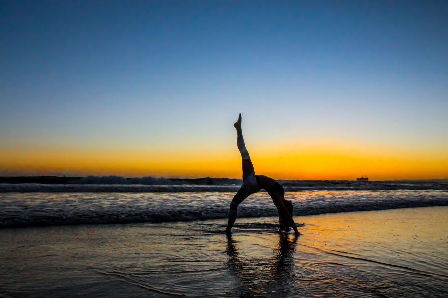 a woman doing yoga on the beach at sunset