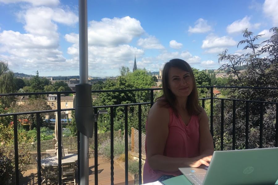 a woman works on a laptop on a balcony overlooking the city of Bath on a sunny day