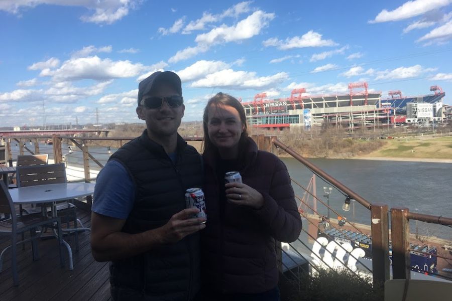 a couple pose for a selfie on a rooftop bar in Nashville. Both hold cans of PBR