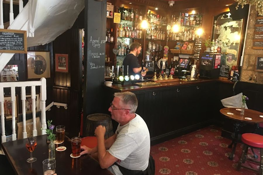 A man drinks a beer inside of a small English opub.