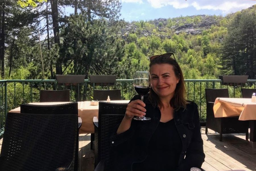 a woman toasts with a glass of red wine in a restaurant surround by lush greenery in Montenegro