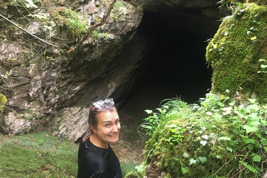 A woman smiles at the entrance to a huge cave opening.