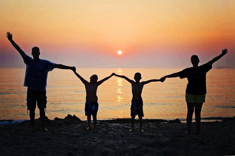 family of 4 silhouette at sunset by the beach