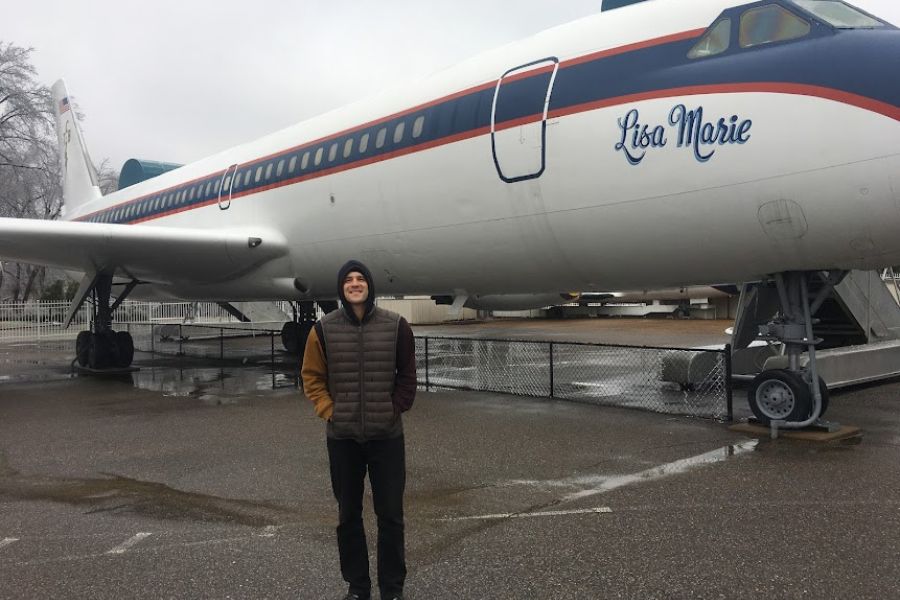 a man wearing numerous layers stands in front of a 747 plane. Written on the side, Lisa Marie' this is Elvis' plane at Graceland.