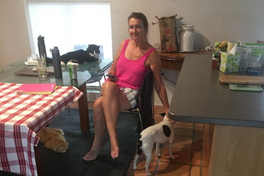 woman sits at table with a dog and 2 cats