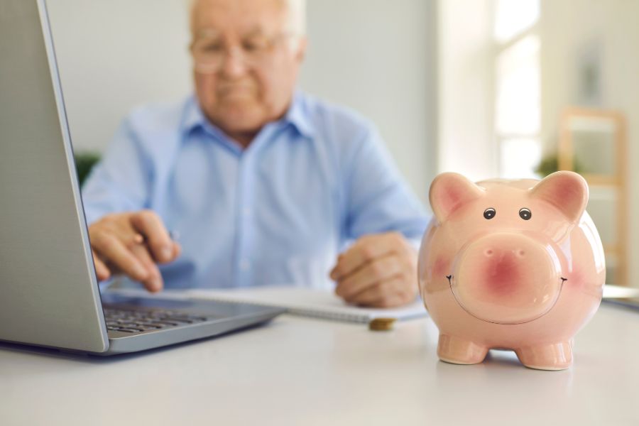 old man at laptop with a piggy bank